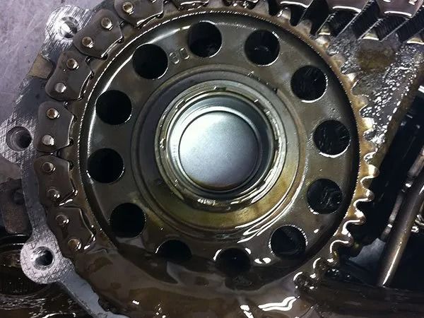 Close-up of engine part with chain and gear, covered in oil.