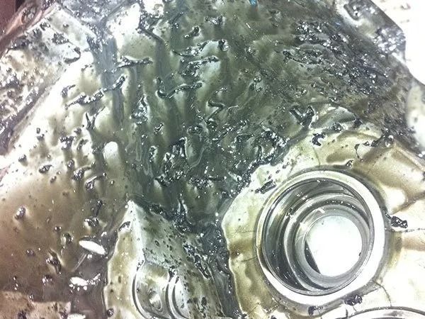 Melted metal surface with dark residue pooling in irregular patterns; a machined hole visible.