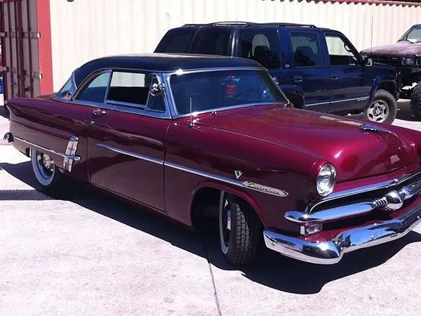 Burgundy and black classic car with chrome details, parked in a lot.