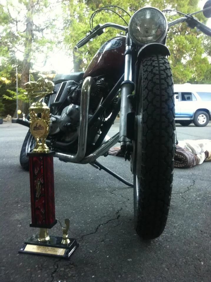 Motorcycle parked next to a trophy; red, black, and chrome details; parked on asphalt.