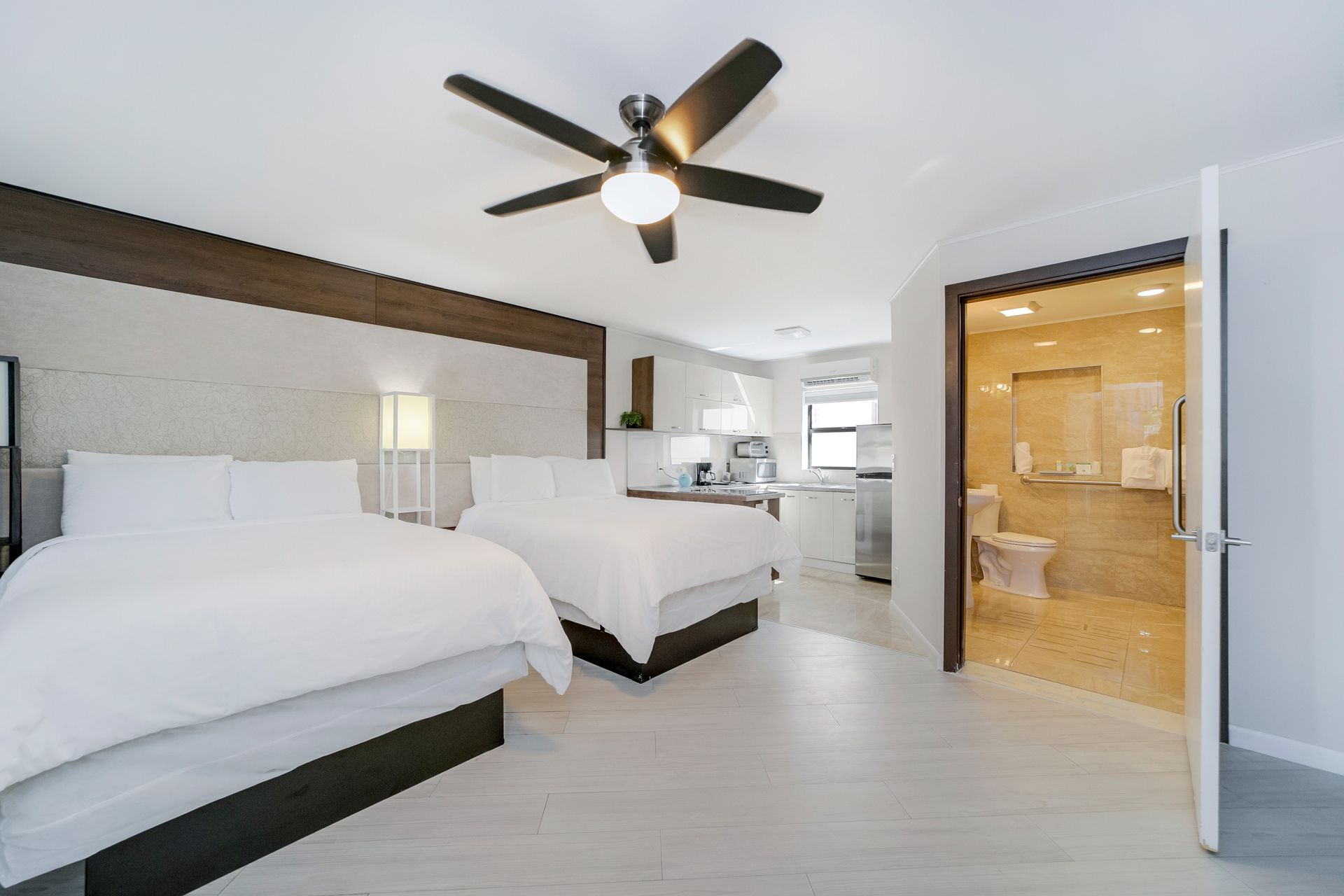 A hotel room with two beds, a small kitchen, and a bathroom. Bright, modern decor.