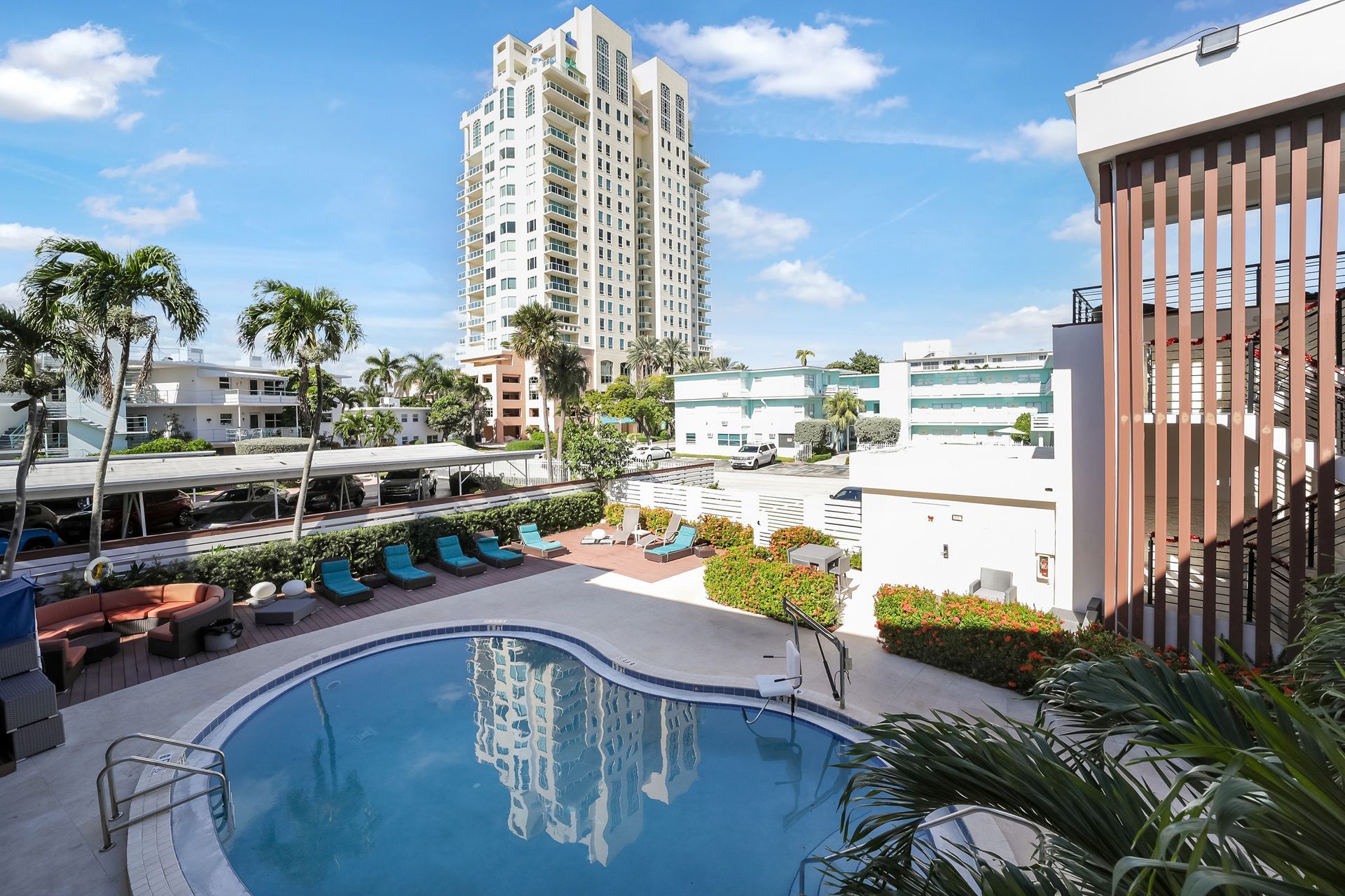 Pool and lounge area with a high-rise building in the background. Blue pool, lounge chairs, and palm trees.