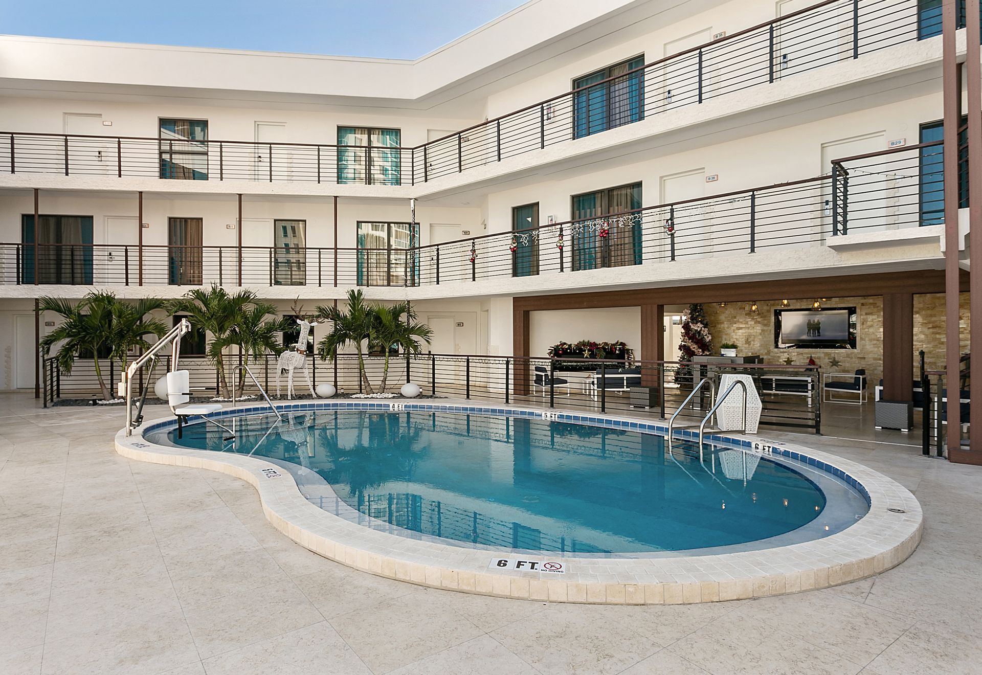 Courtyard hotel with pool. White building with black railings, turquoise pool, palm trees.