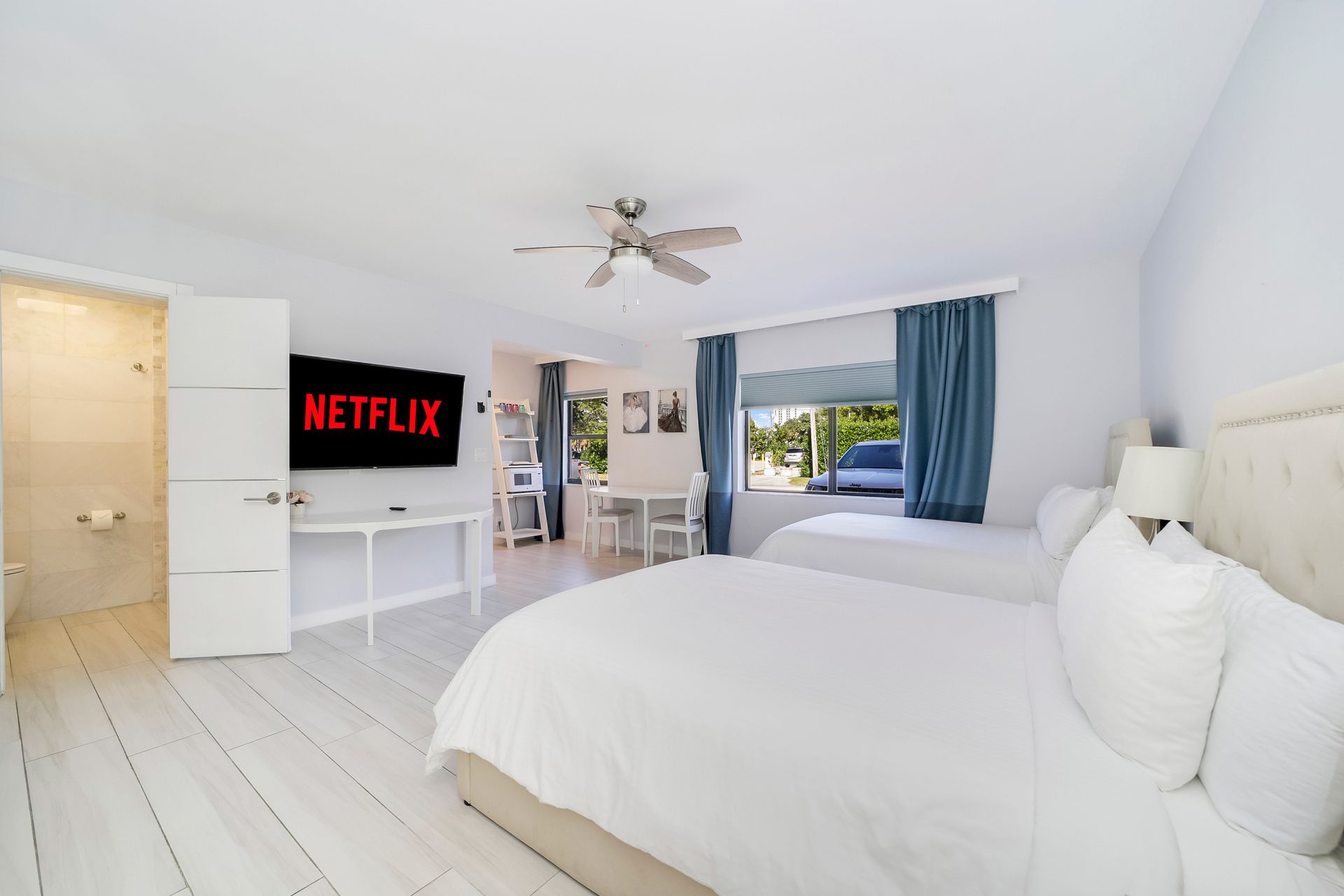 Bedroom with two beds, large TV with Netflix, window with curtains, and dining table.