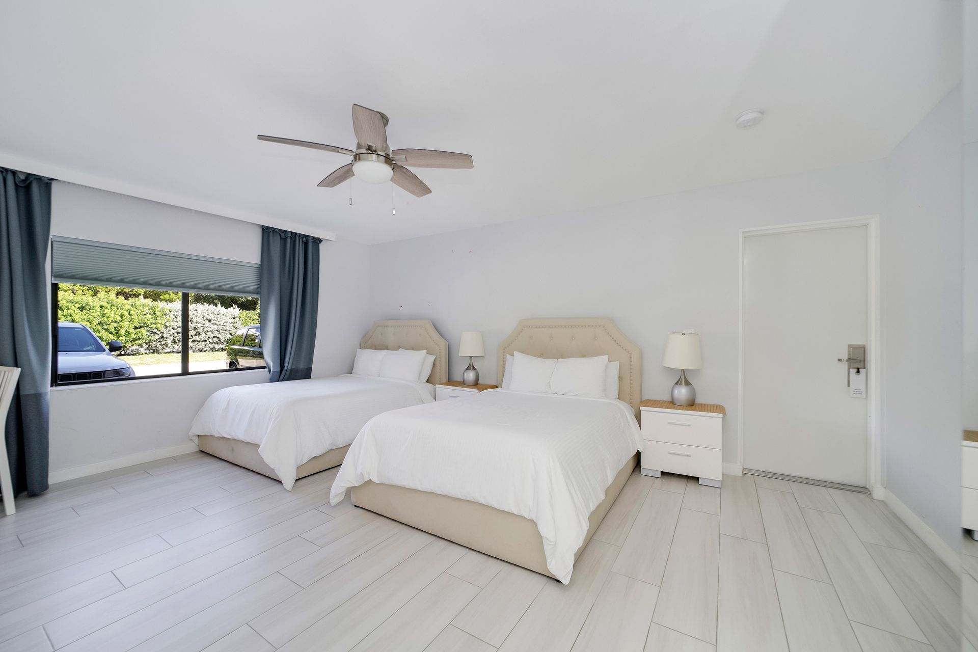 A bright bedroom with two twin beds, a window, and a ceiling fan.