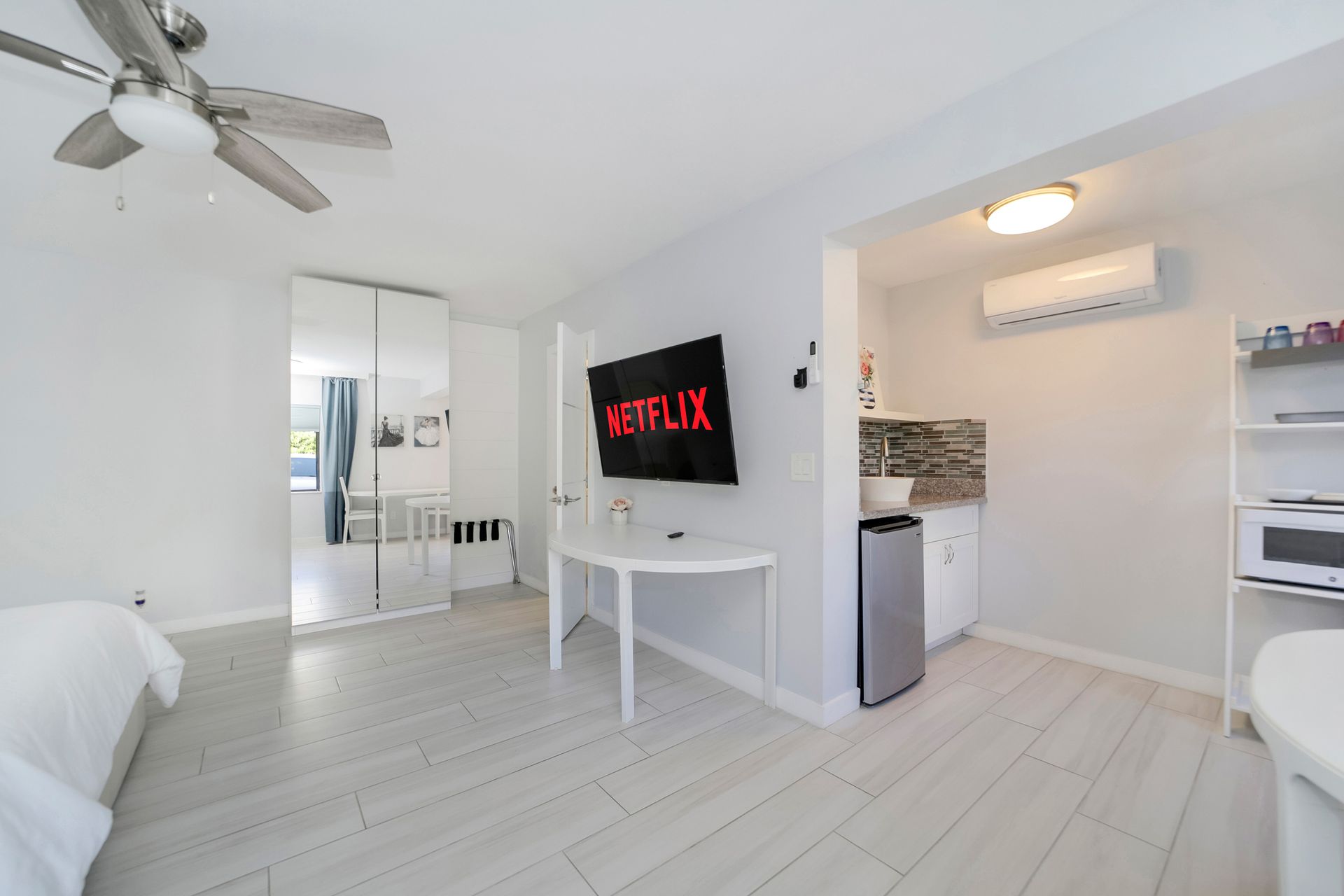 Bright studio apartment with TV, small kitchen, white walls, and wood-look floors.