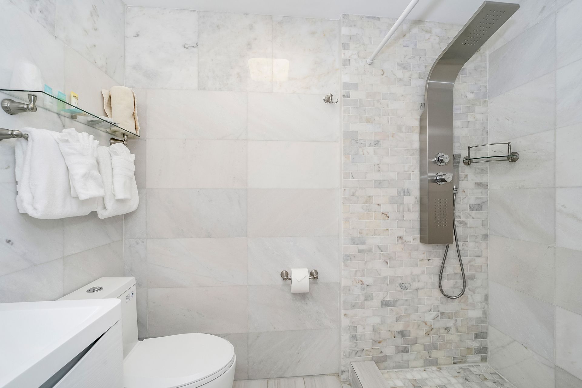 White marble bathroom with toilet, shower, and towel rack.