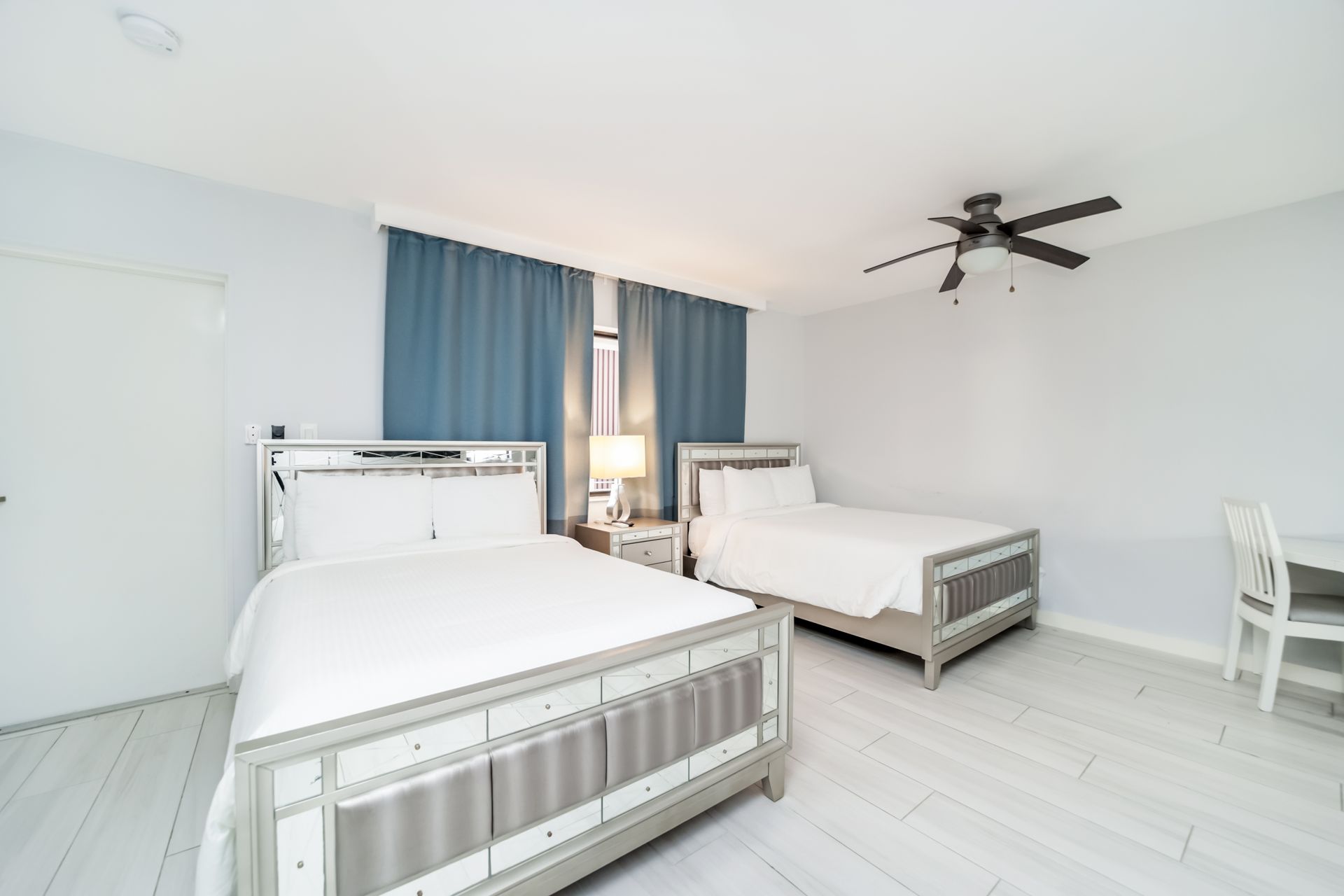 Bedroom with two beds, white decor, blue curtains, and ceiling fan.