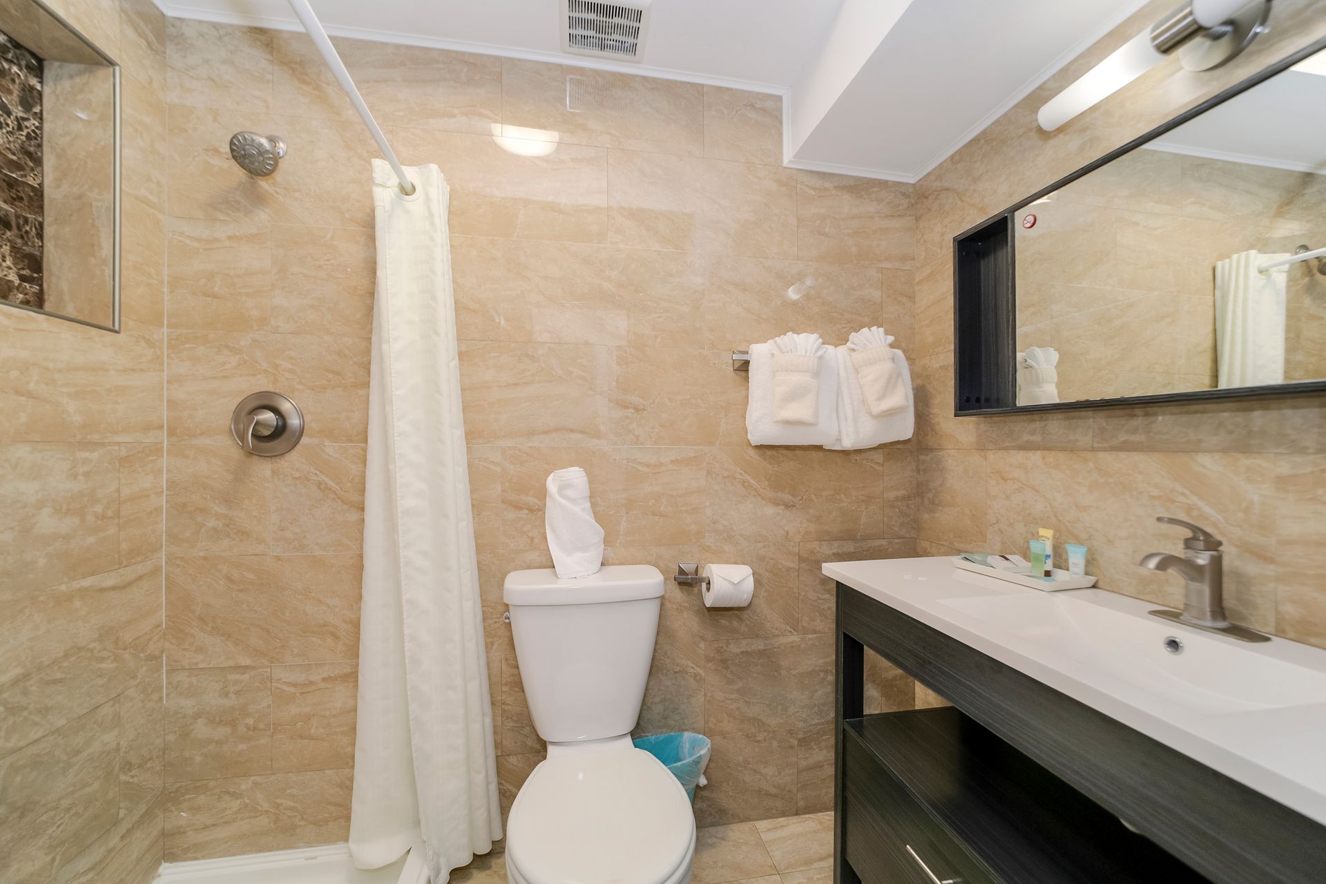 Bathroom with beige tiled walls, a toilet, vanity, and shower with a white curtain.