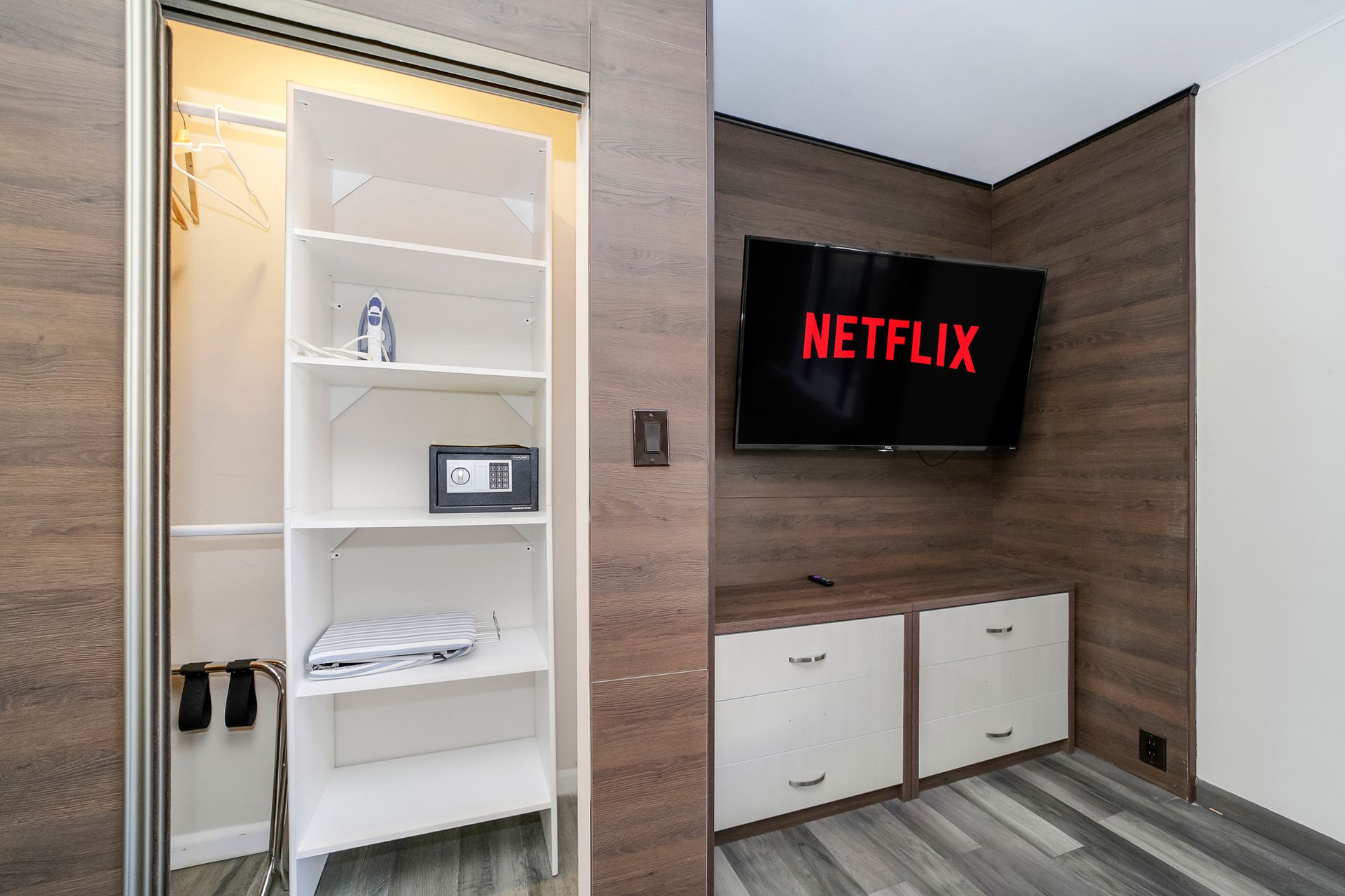 Closet with open shelves, safe, and TV with Netflix logo above white cabinets in a room.