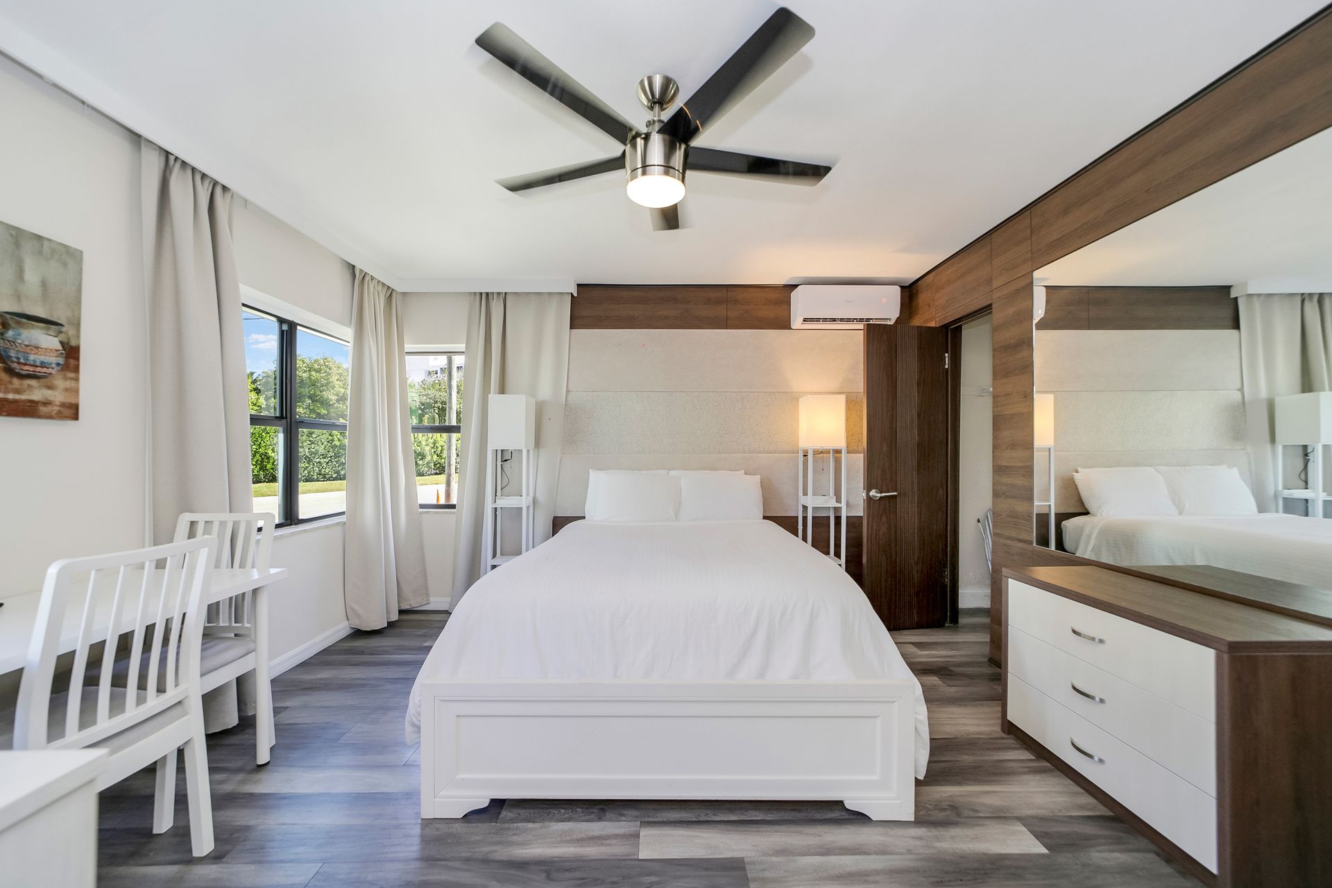 Bedroom with white bed, gray flooring, desk, dresser, and ceiling fan.