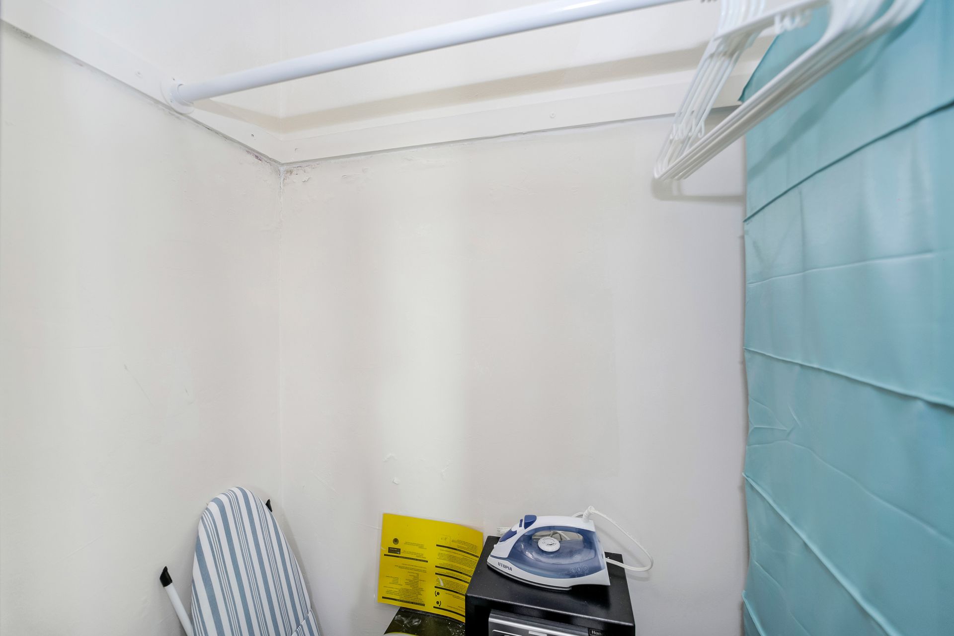 Small laundry room with ironing board, iron, and hanging rod.