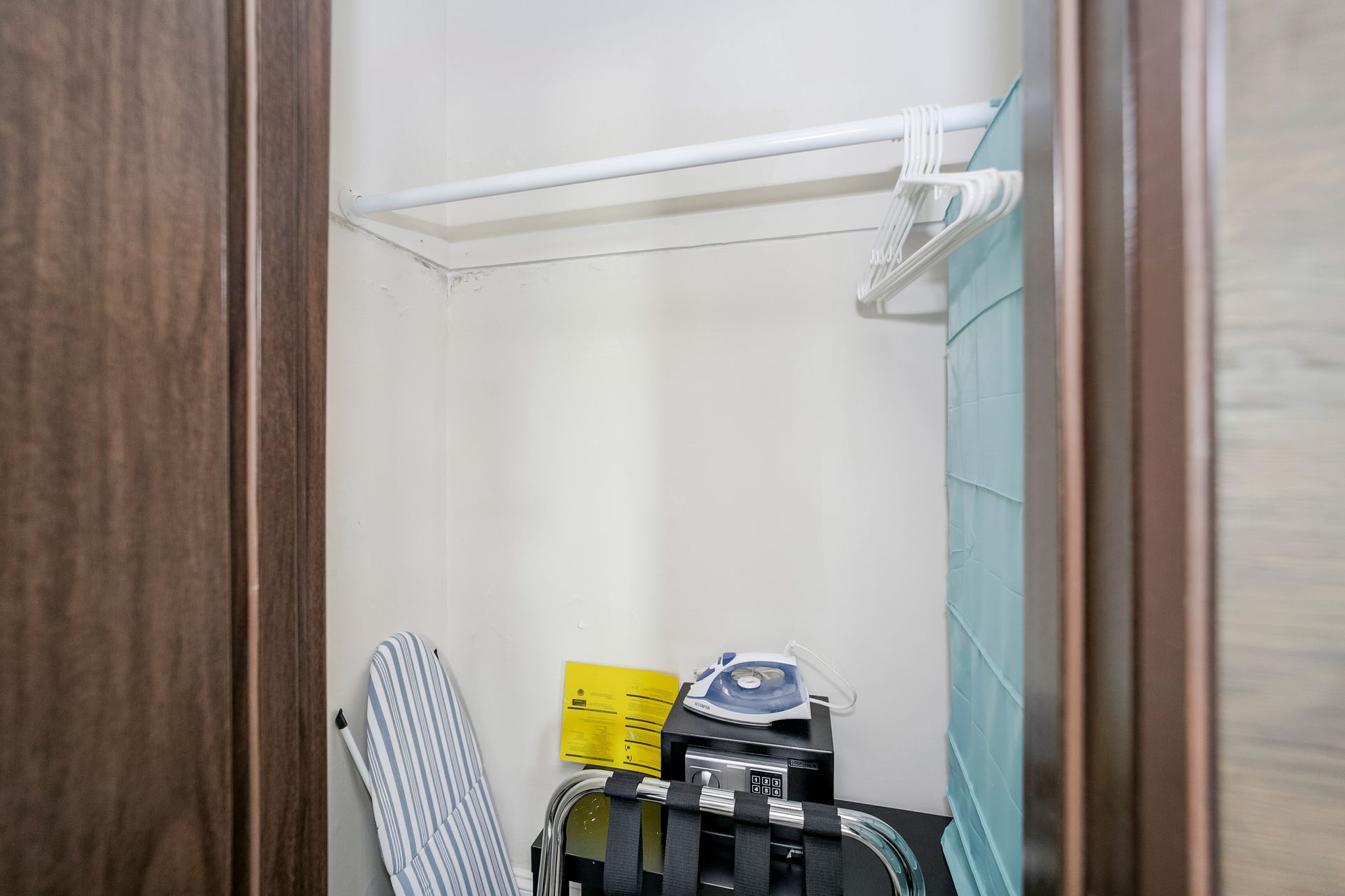 Closet with hanging rod, ironing board, luggage rack, iron, and hangers.