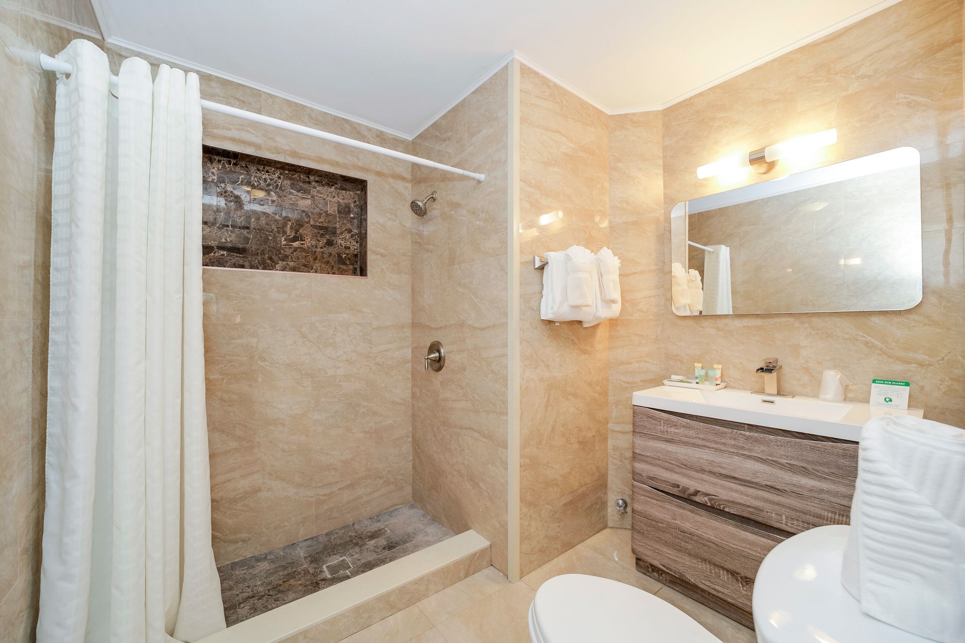 Bathroom with tiled walls, shower with curtain, vanity, mirror, and toilet.