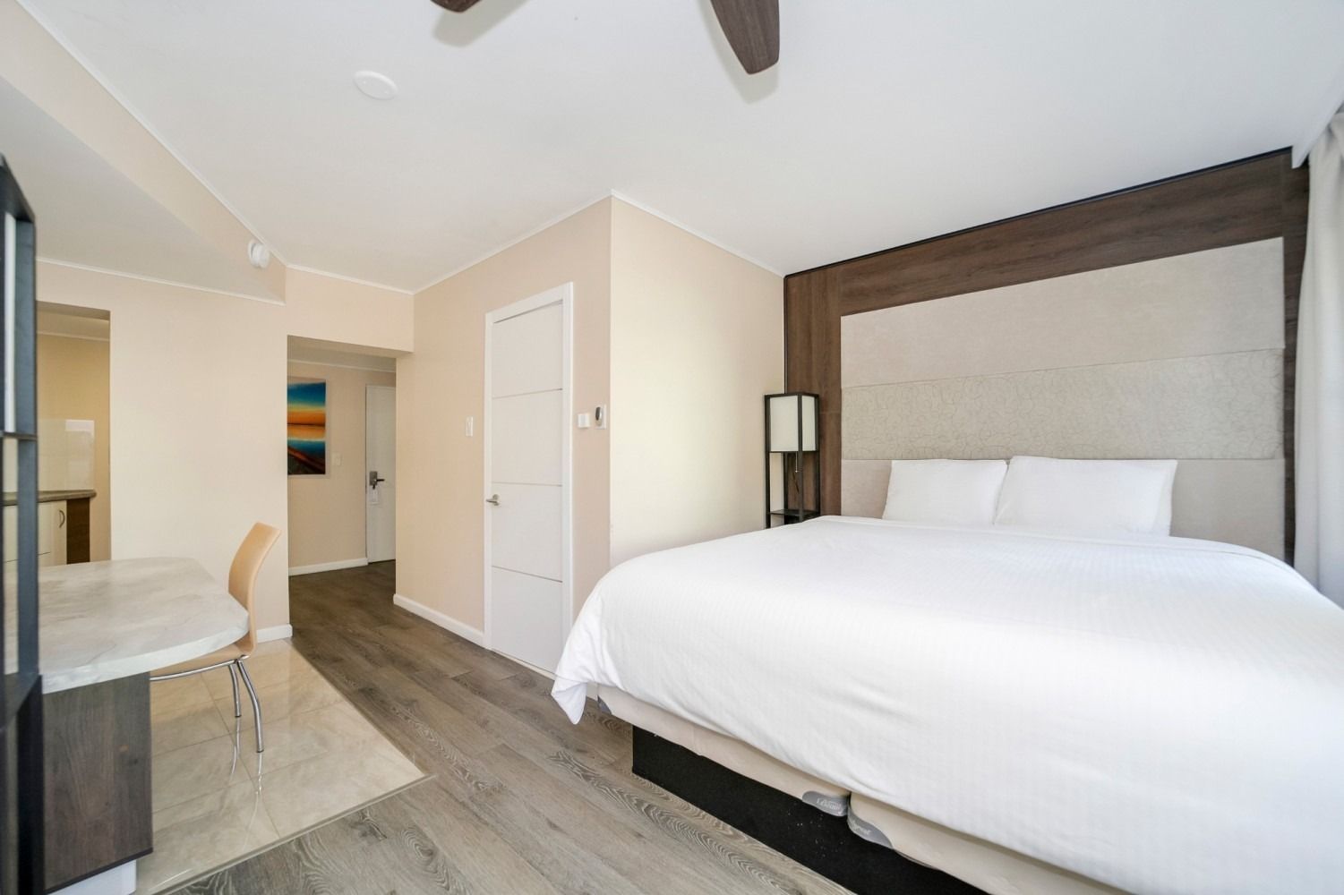 Bedroom with bed, desk, and doorway. Wooden floors and headboard. Neutral colors and a modern design.
