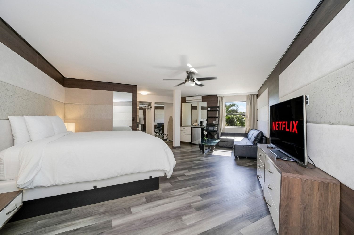 Spacious studio with bed, sofa, TV displaying Netflix, and a modern bathroom area.
