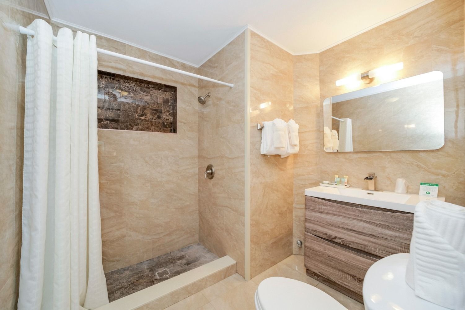 Bathroom with tan tile, shower with curtain, vanity, mirror, and toilet.