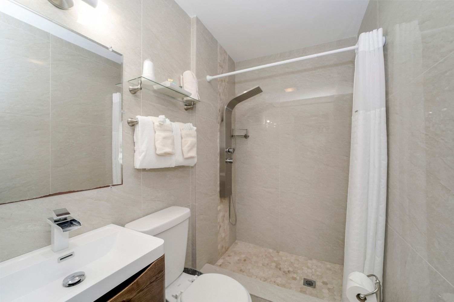 Bathroom with a white vanity, toilet, and shower. Gray tile walls and a white shower curtain.