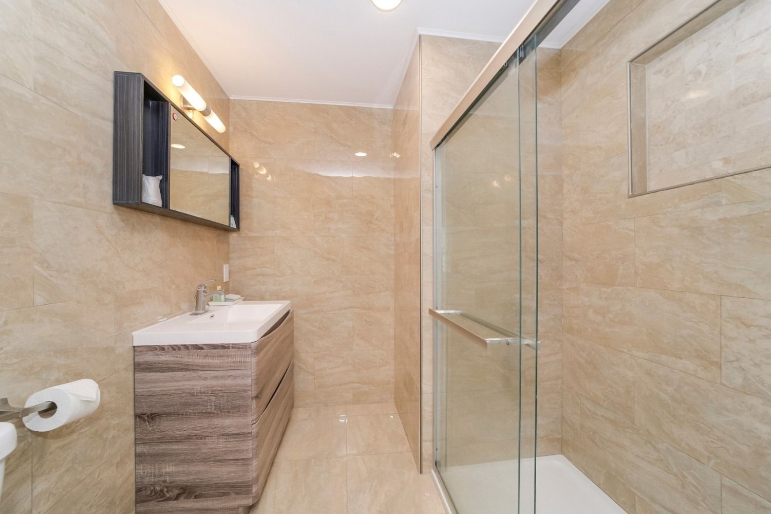 Bathroom with tan tile walls, wood vanity, mirrored medicine cabinet, and glass shower.