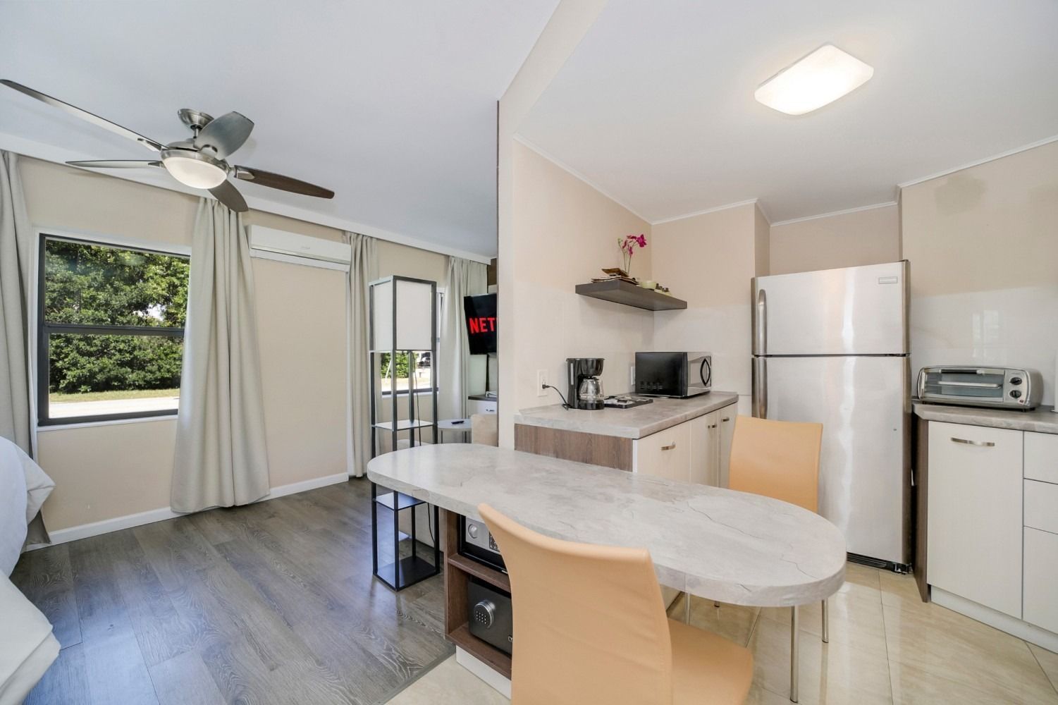 Studio apartment with kitchen, dining area, and large window; light wood floors and white walls.