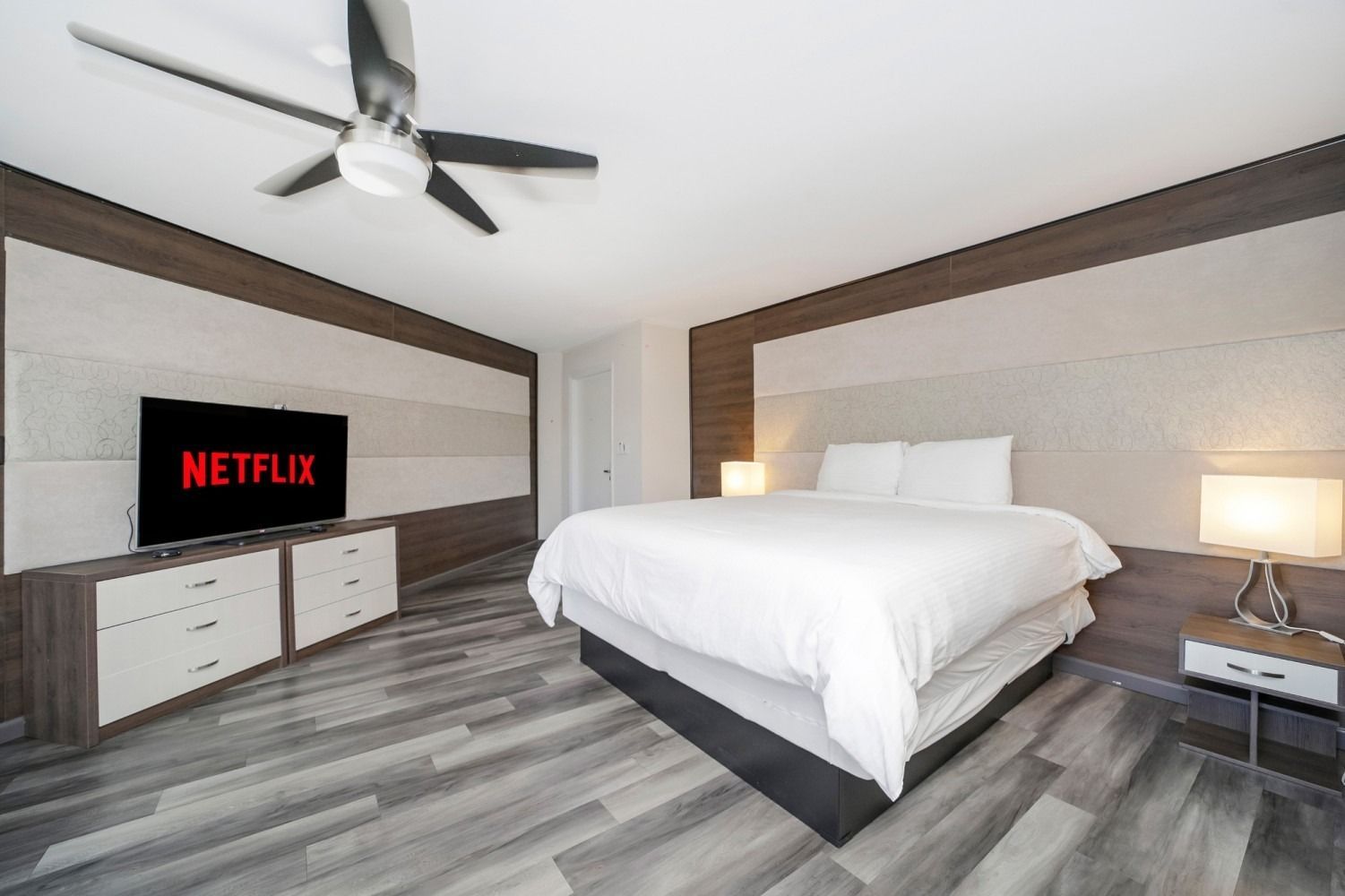 Bedroom with king-sized bed, TV with Netflix logo, wooden accents, and gray flooring.