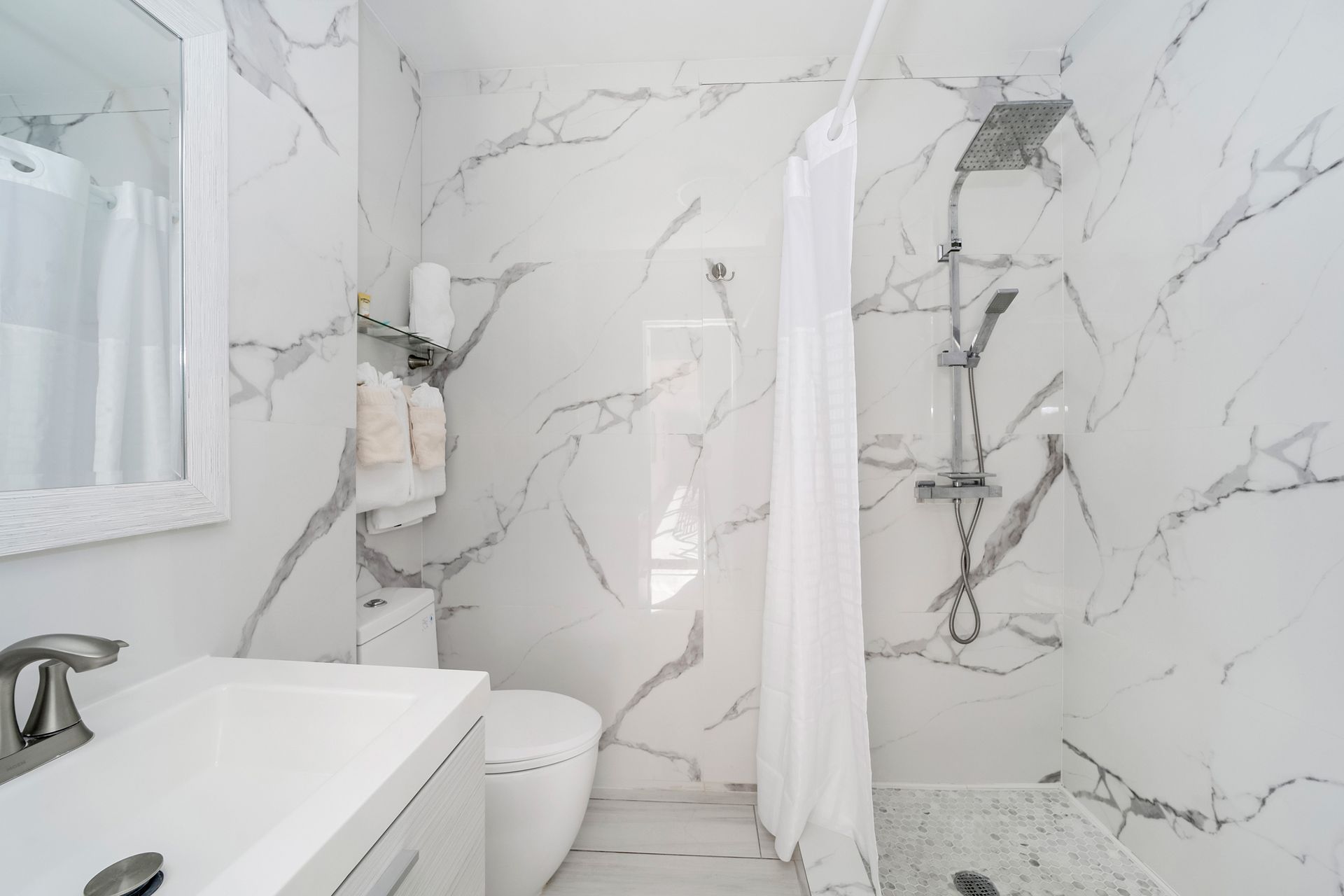 White marble bathroom with shower, toilet, and sink.