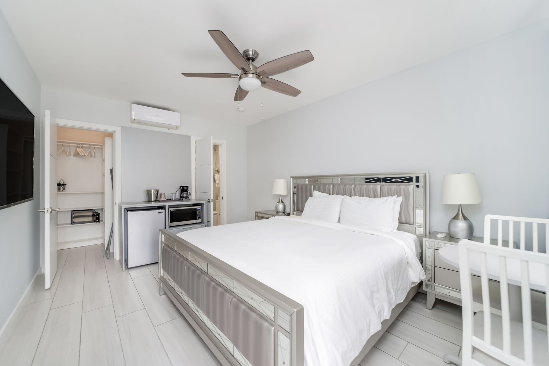 Bedroom with bed, desk, closet, and appliances, in a light-colored, minimalist style.
