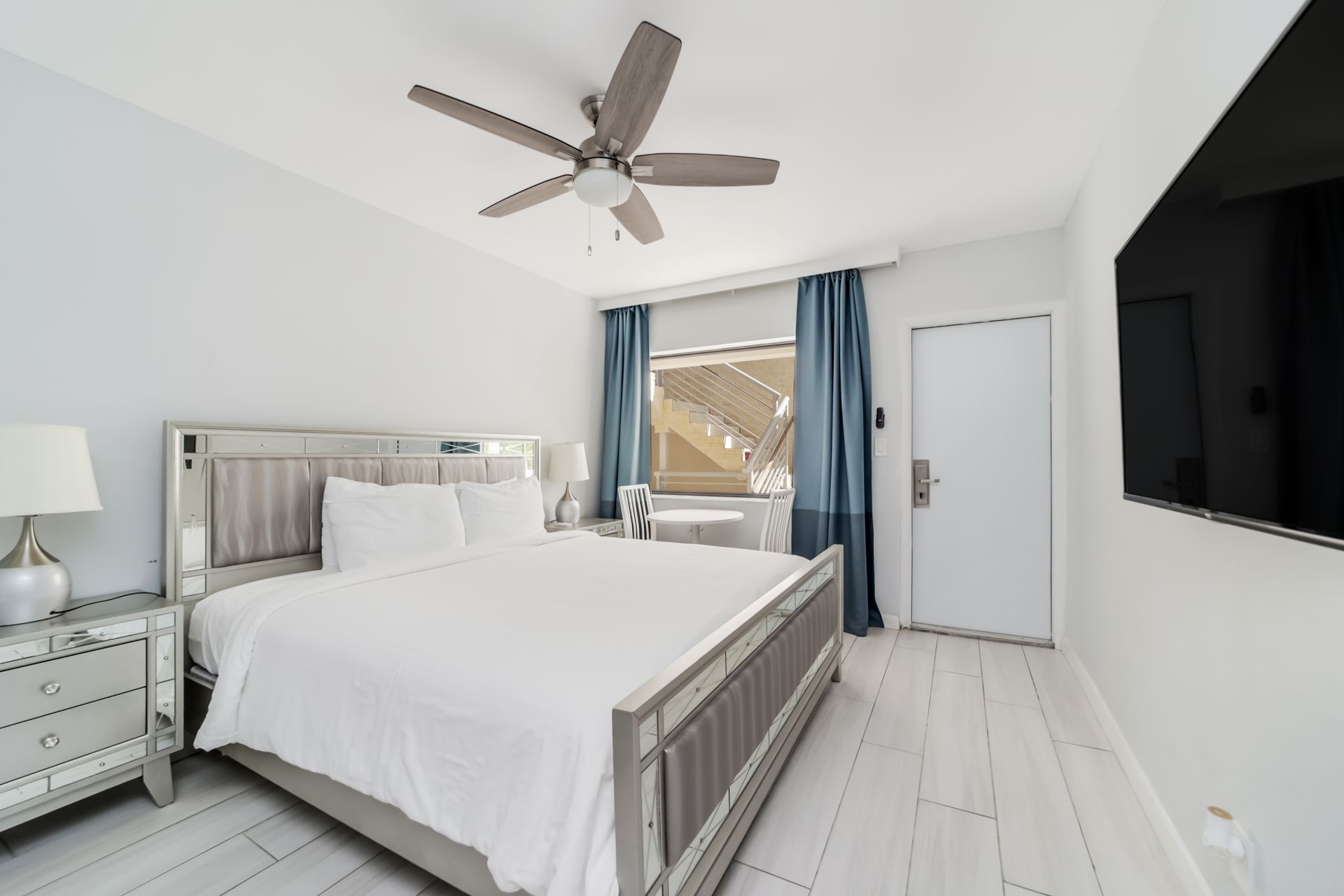 Bedroom with a mirrored bed frame, white bedding, and a ceiling fan.