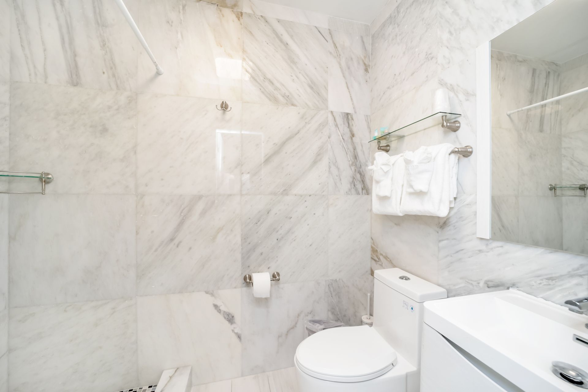 White marble bathroom with a toilet, sink, shower, and towels.
