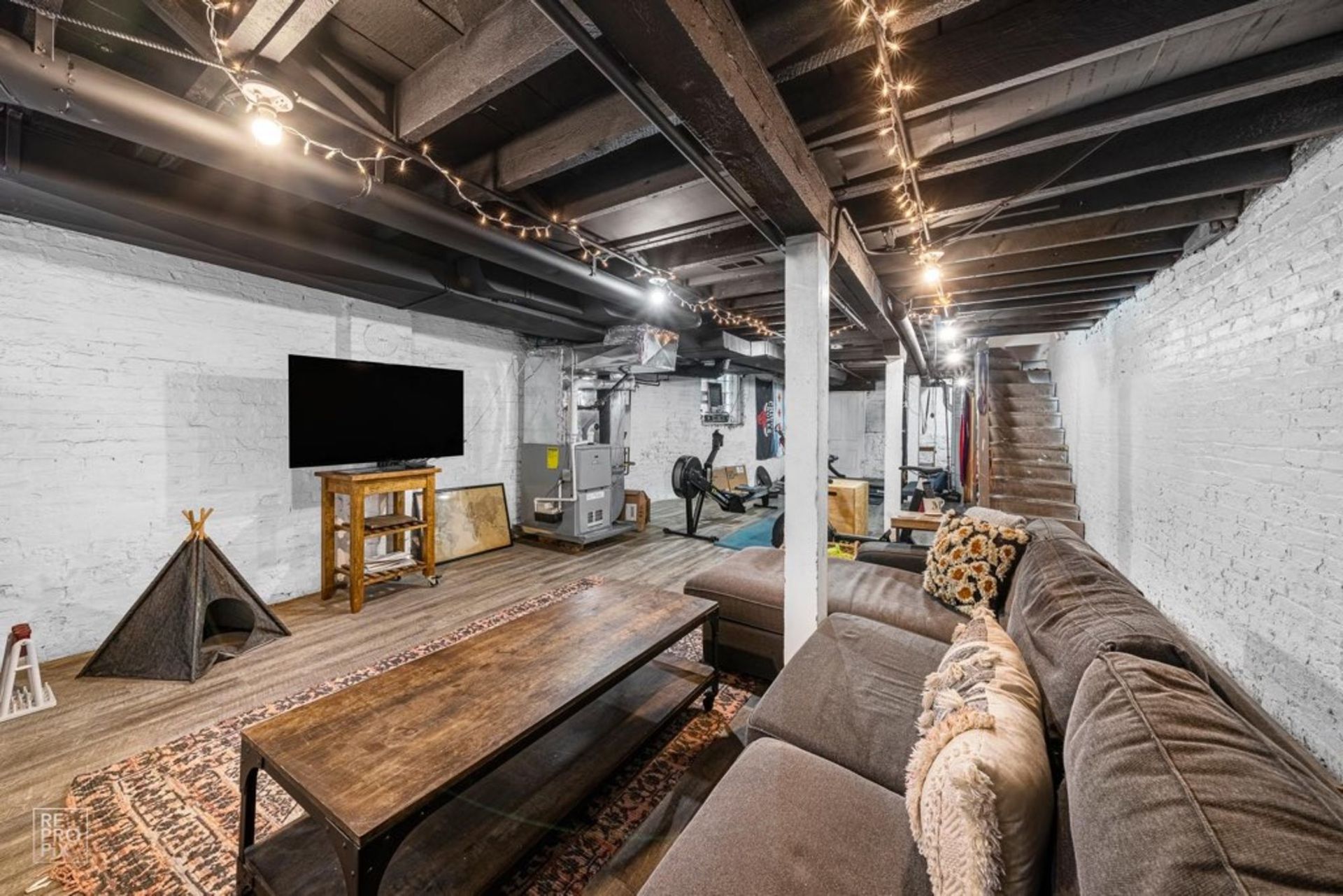 A living room in a basement with a couch and a flat screen tv.