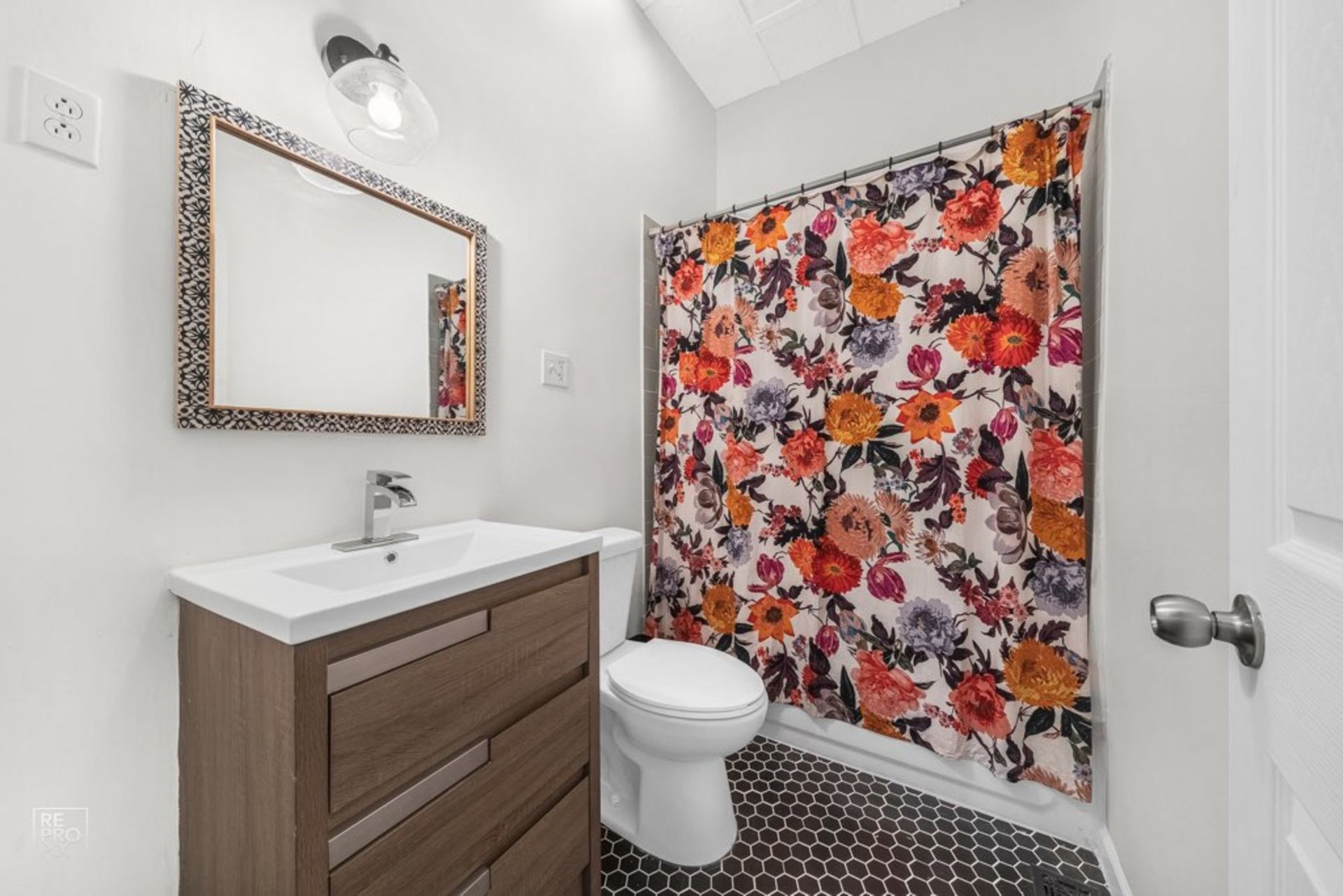 A bathroom with a toilet , sink , mirror and shower curtain.