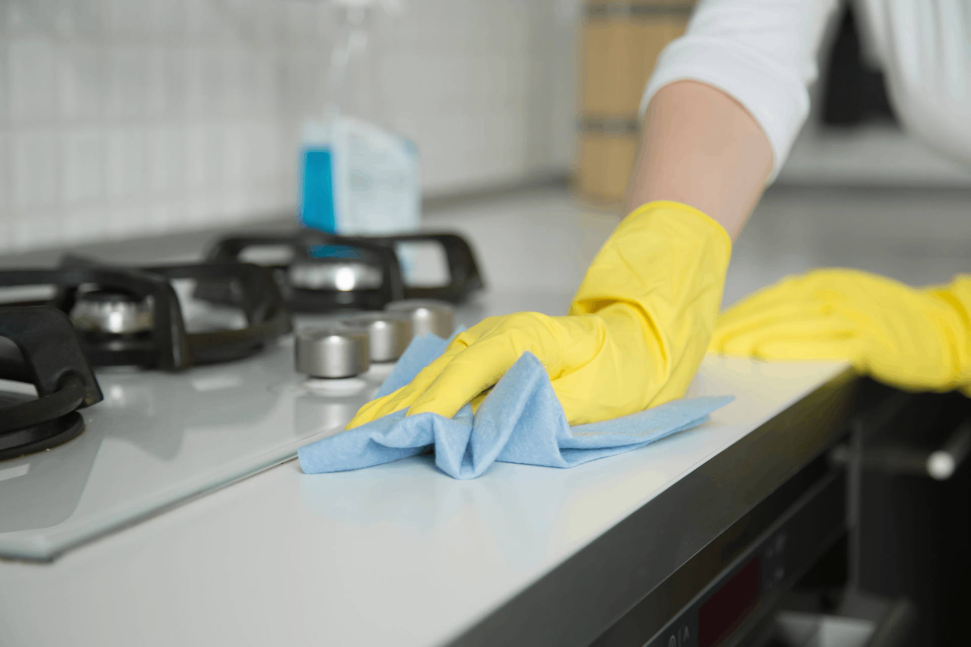 A person wearing yellow gloves is cleaning a stove top with a cloth.