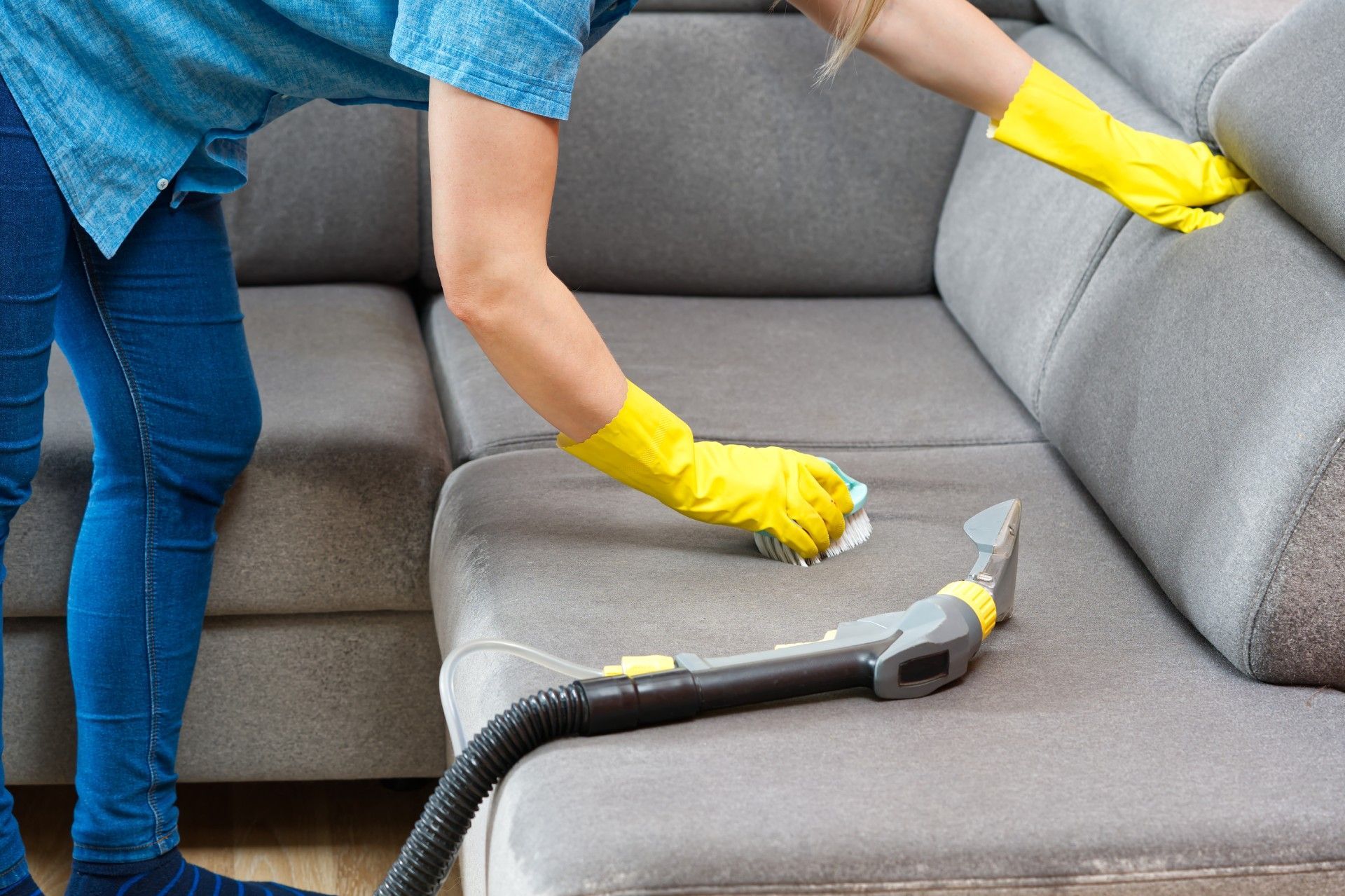 A woman is cleaning a couch with a vacuum cleaner.