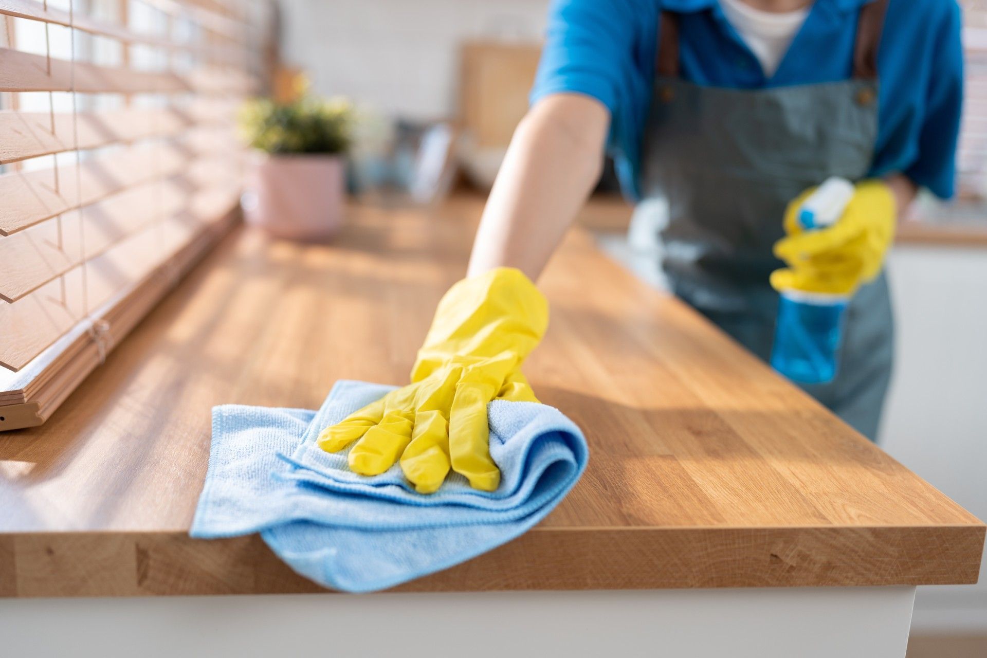 A person wearing yellow gloves is cleaning a wooden counter top with a cloth.