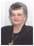 An older woman wearing glasses and a necklace is smiling for the camera.