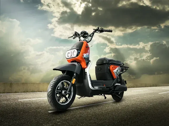 Patinete eléctrico naranja y negro en una carretera, fondo de cielo nublado.