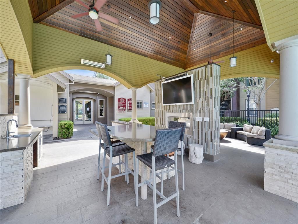 Outdoor covered amenity area with a tall table, seating, grill, and mounted TV.