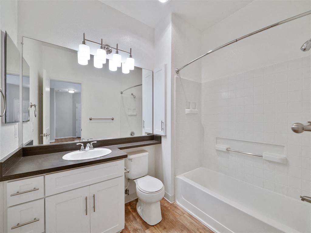 Bathroom in an apartment with a vanity, toilet, and tub/shower with grab bars.