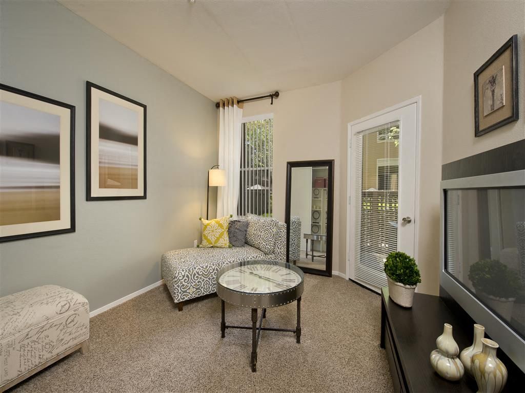 Living room with a gray patterned chair, round glass coffee table, mirror, and French doors.