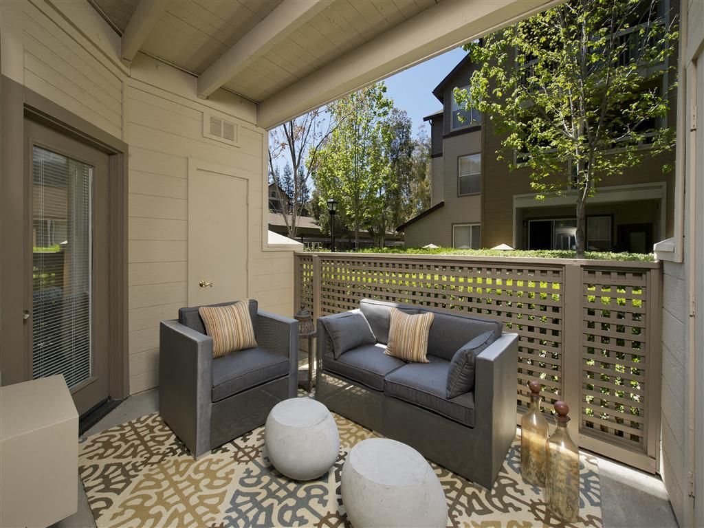 Outdoor apartment balcony with gray seating, cushions, and lattice railing.