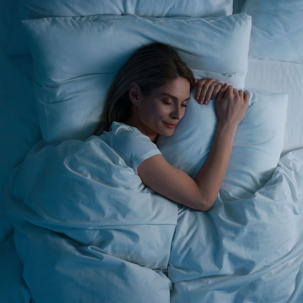 A woman is sleeping in a bed with white sheets and pillows