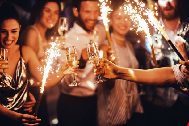 A group of people are holding sparklers and glasses of champagne at a party.