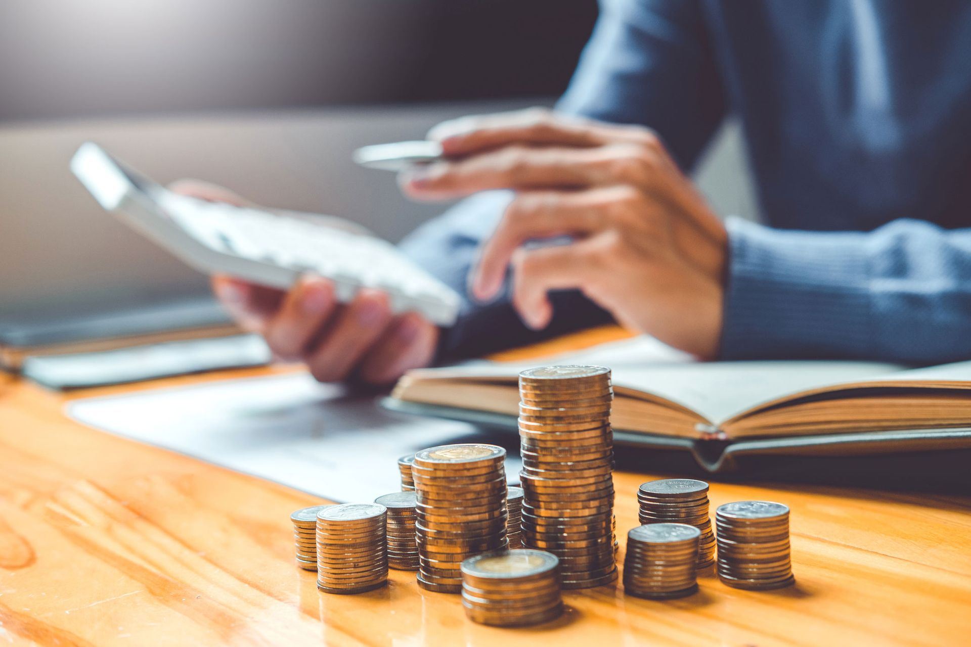 A person is using a calculator while sitting at a table with stacks of coins.