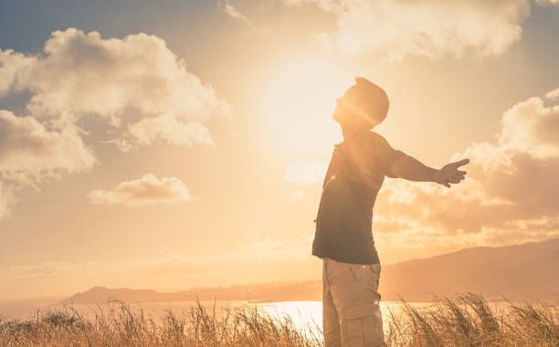 A man is standing in a field with his arms outstretched at sunset.