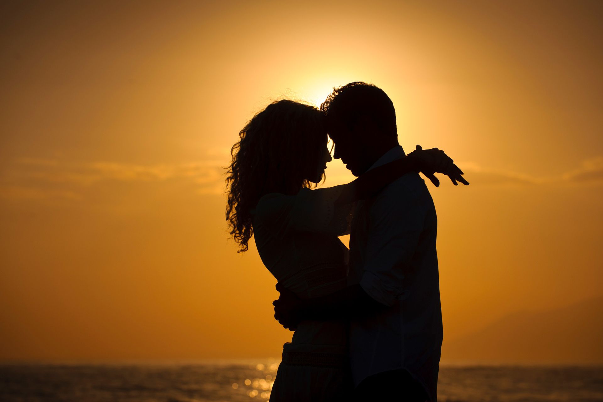 A man is kissing a woman on the forehead on the beach.