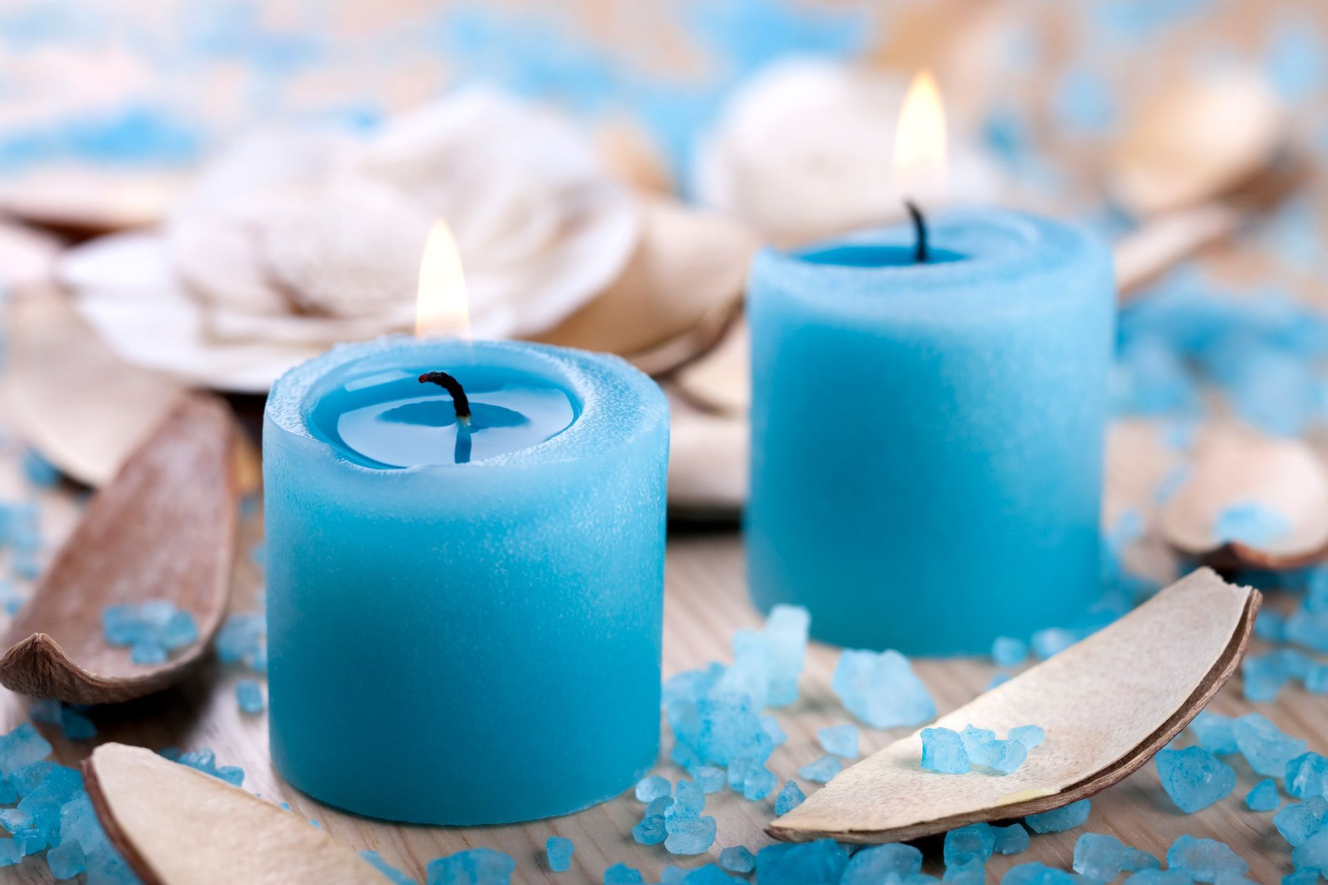 Two blue candles are sitting on a wooden table next to sea salt.