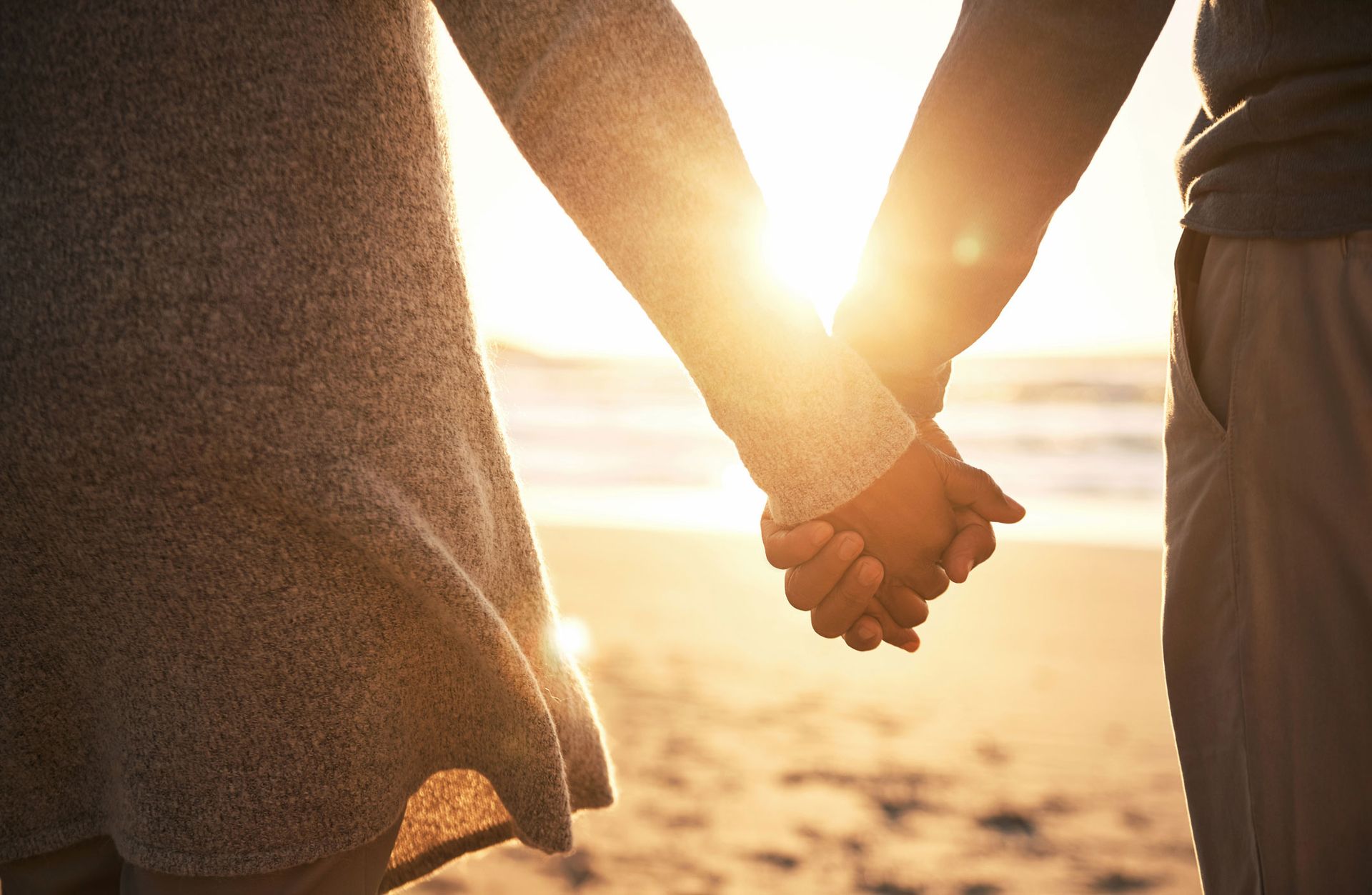 A man and a woman are holding hands on the beach at sunset.