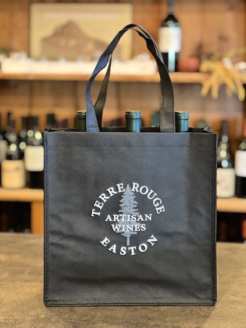 Black wine tote bag with the Terre Rouge Artisan Wines logo, holding bottles. Wooden background.