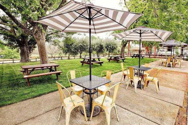 A patio with tables and chairs under striped umbrellas and picnic tables.
