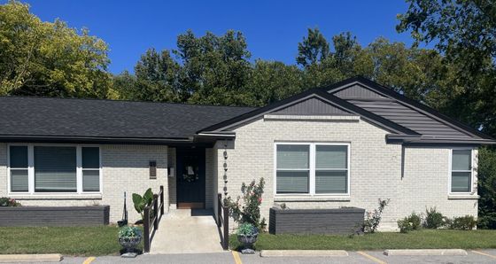 A white brick house with a black roof and a handicap ramp.